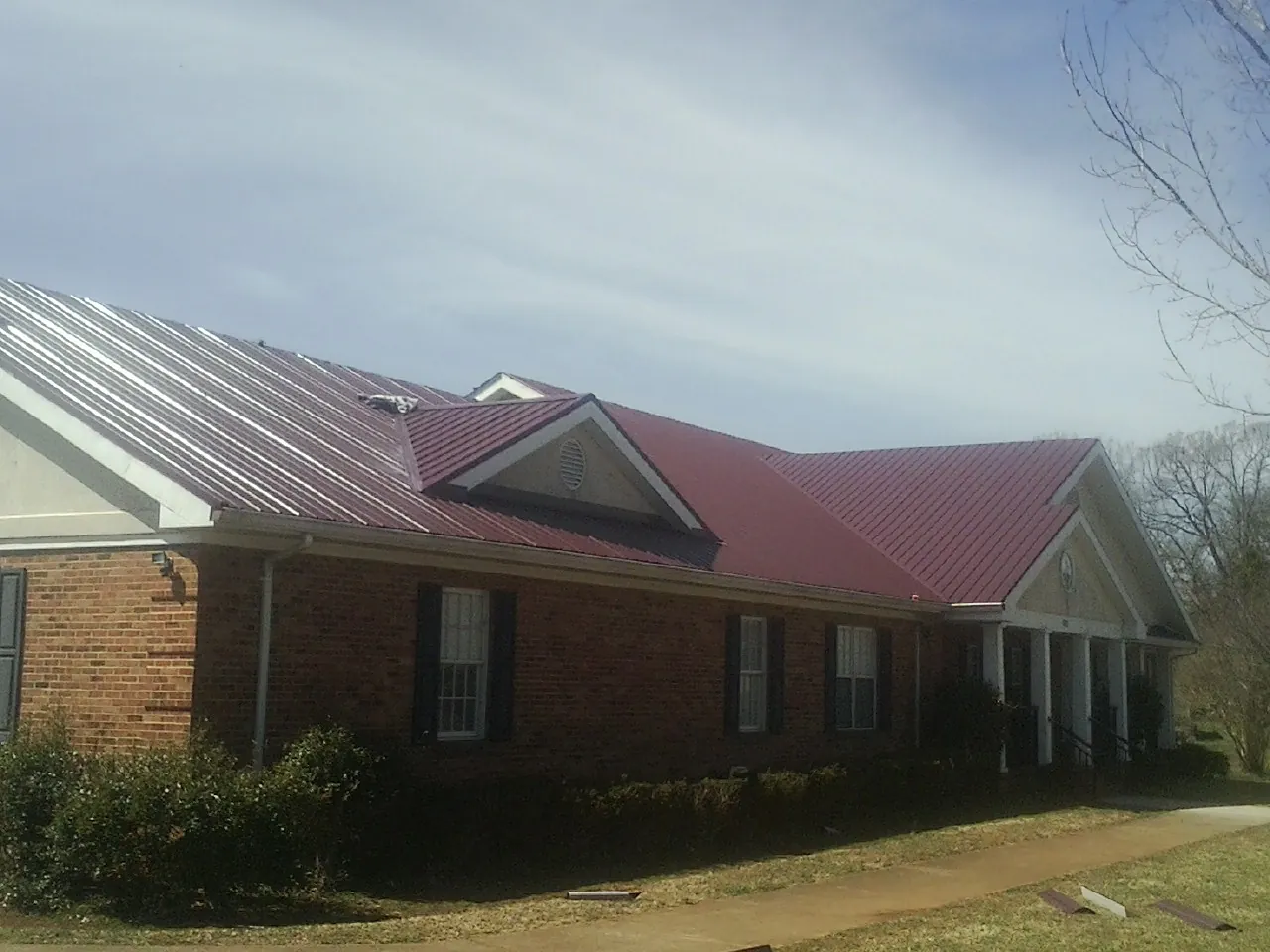Red metal roof with gabled entries on a long brick building, from a Hail Damage Roof Repair job in Cusseta