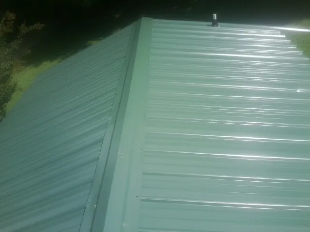 New green metal panels meeting at the ridge of a roof — Flat Roof Repair work by our crew in Cusseta