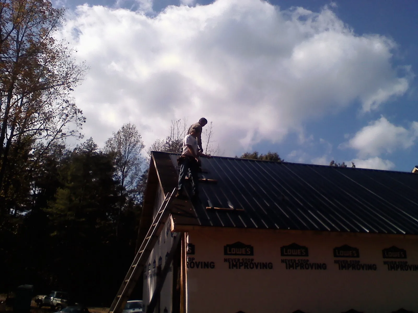 Roofer fastening dark metal panels high against a cloudy sky, from a Roof Inspection job in Cusseta