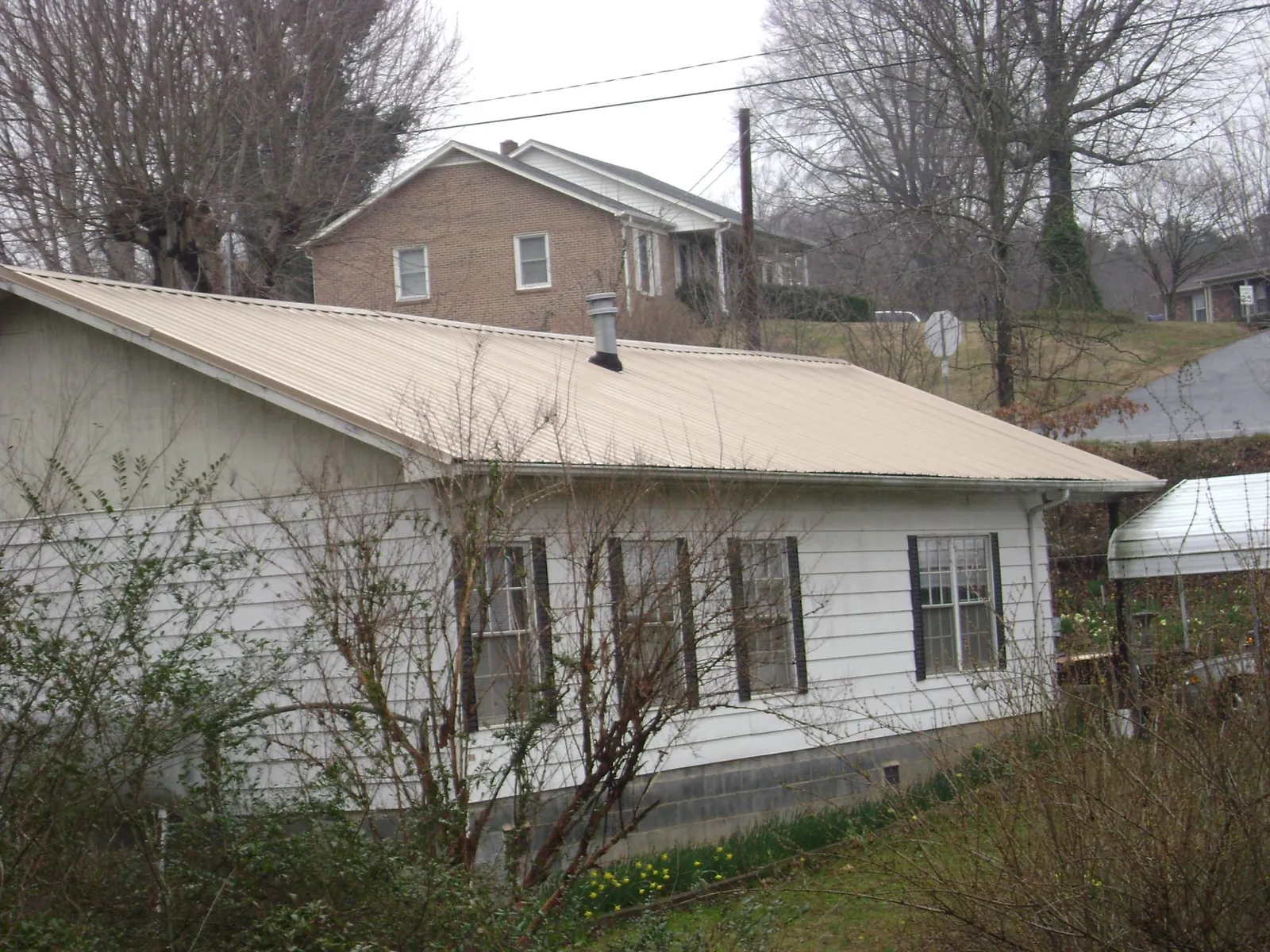 Tan metal roof on a white sided house set into a hillside — Commercial Roofing by Roofing Brothers in Cusseta