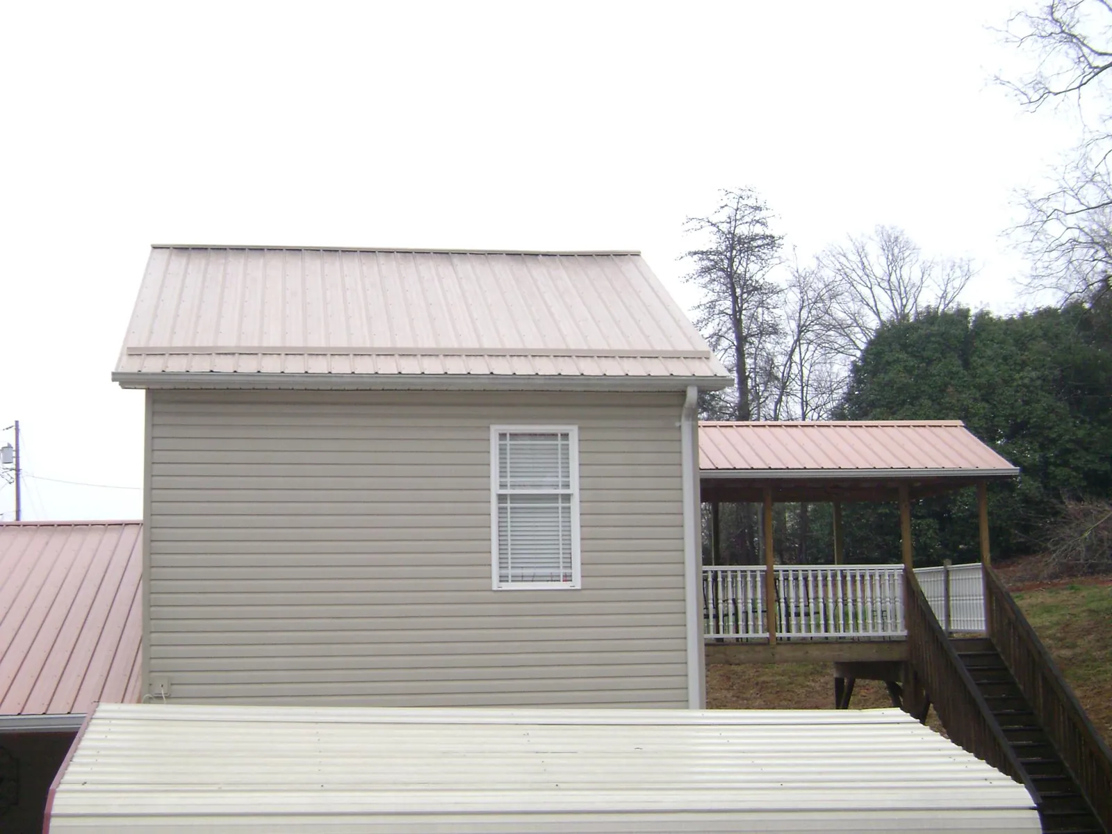 Tan metal roofs on a two story addition and attached porch, from a Roof Replacement job in Cusseta